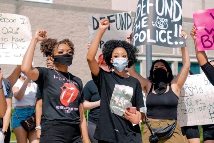 Protesters with a sign "Defund the police." Photo by Andrew Robinson on Unsplash