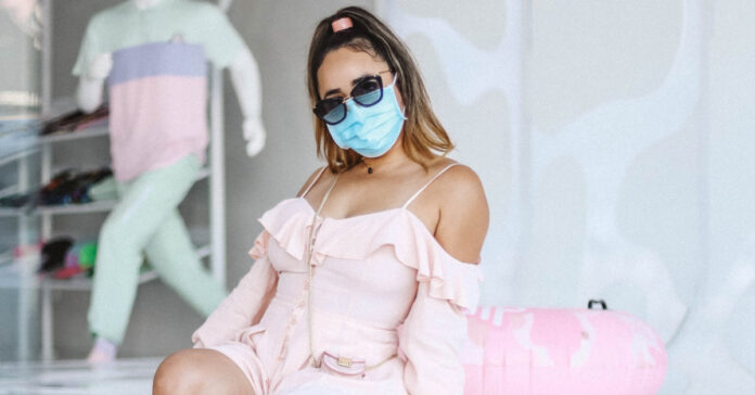 Woman in pink dress, blue mask, and sunglasses in California. Photo by kevin turcios on Unsplash.