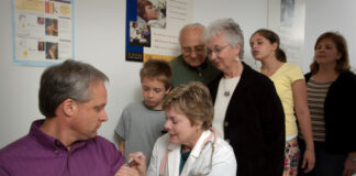 A medical professional gives a man a vaccine while his family watches.