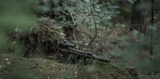 Shooter in ghilliesuit with a suppressed rifle.