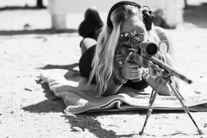 A female shooting a scoped precision rifle.