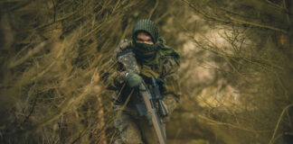 A rifle-toting soldier in camo in the woods.