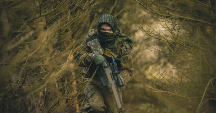 A rifle-toting soldier in camo in the woods.