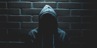 A person in a hoodie with their face obscured by shadows.