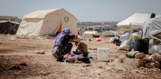 A Syrian woman bathes a young boy in a refugee camp