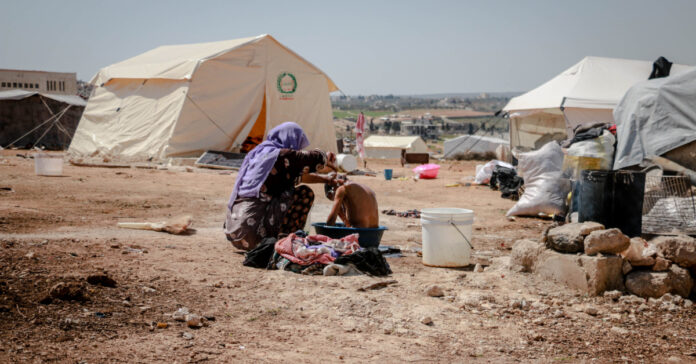 A Syrian woman bathes a young boy in a refugee camp