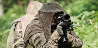 Two armed men in camouflage in the woods.