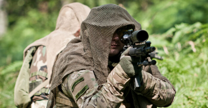 Two armed men in camouflage in the woods.