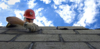 A man in a hard hat builds a cinder block wall.