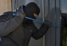 A burglar uses a pry bar to break into a building.