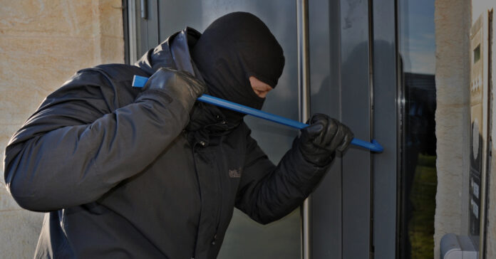 A burglar uses a pry bar to break into a building.