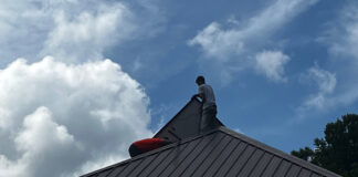 An installer positions a solar panel on the other side of the roof ridgeline,