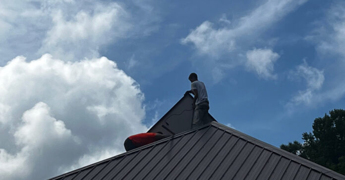 An installer positions a solar panel on the other side of the roof ridgeline,