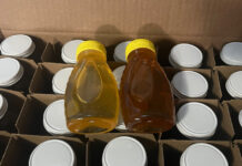 Two 8-ounce bottles of freshly harvested honey sitting on top of a box of two-dozen one-pound jars.