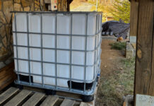 The IBC Tote positioned outside the house near our solar inverter and a woodpile. When filled with water, this will give us 275 gallons of water for firefighting.