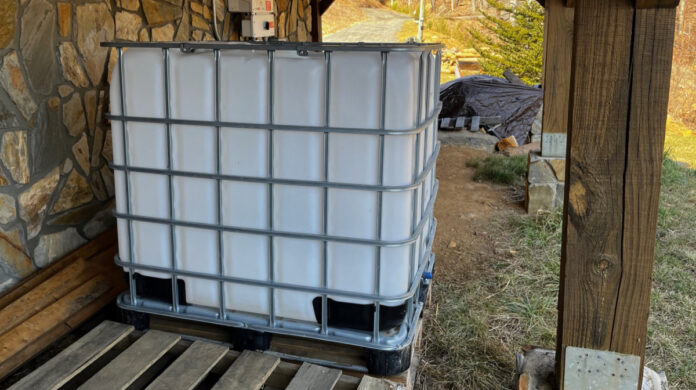 The IBC Tote positioned outside the house near our solar inverter and a woodpile. When filled with water, this will give us 275 gallons of water for firefighting.